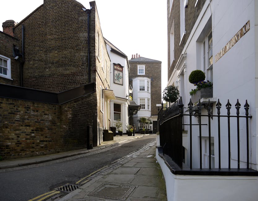 A narrow staircase leading from an interior space to an outdoor area, with a wooden railing on the right side and a concrete wall on the left. The outdoor section features a small balcony or landing w